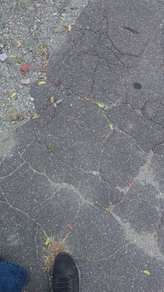 Phone pointed straight down at shoes on asphalt